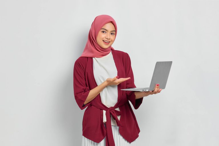 Confident woman in hijab presenting laptop in a modern setting.
